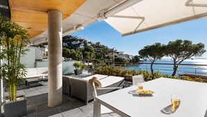 An outdoor patio with a white table, wicker chairs, and a view of the sea and hills. - Beachfront two-bedroom apartment with sea views in Canyelles Petites (Roses)