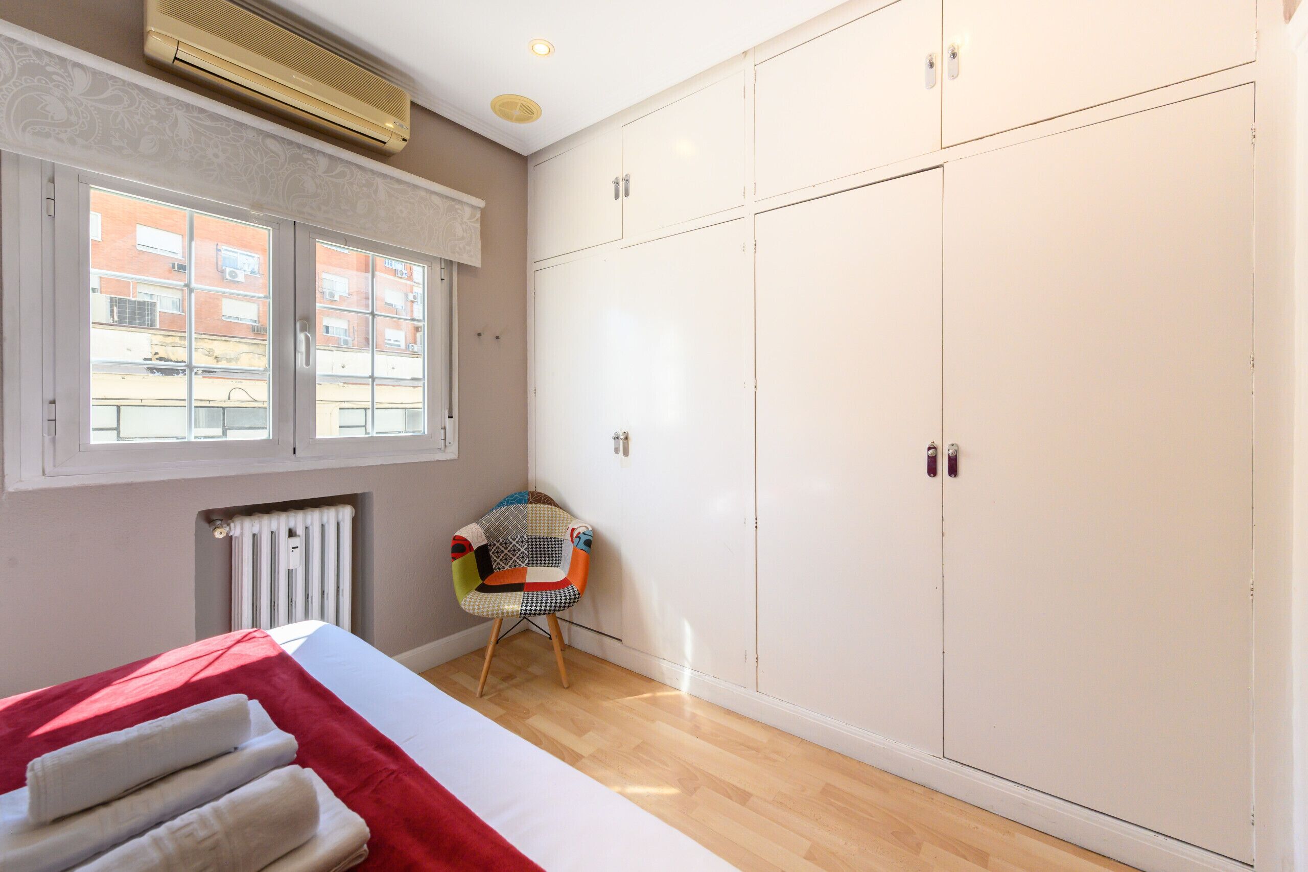 A room with a bed, a radiator, a window, a chair, and a wardrobe.