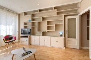 A modern living room with built-in shelving, a flat-screen TV, a small table with a magazine, and a colorful chair. - Cozy Apartment Madrid. Bº SALAMANCA, IFEMA. AEROPUERTO. 2 ROOMS- 6 PAX - ELEVATOR (Madrid)