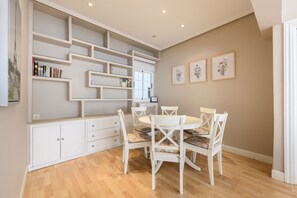 A dining area with a white table and chairs, a built-in bookshelf, and framed floral artwork on the wall. - Cozy Apartment Madrid. Bº SALAMANCA, IFEMA. AEROPUERTO. 2 ROOMS- 6 PAX - ELEVATOR (Madrid)