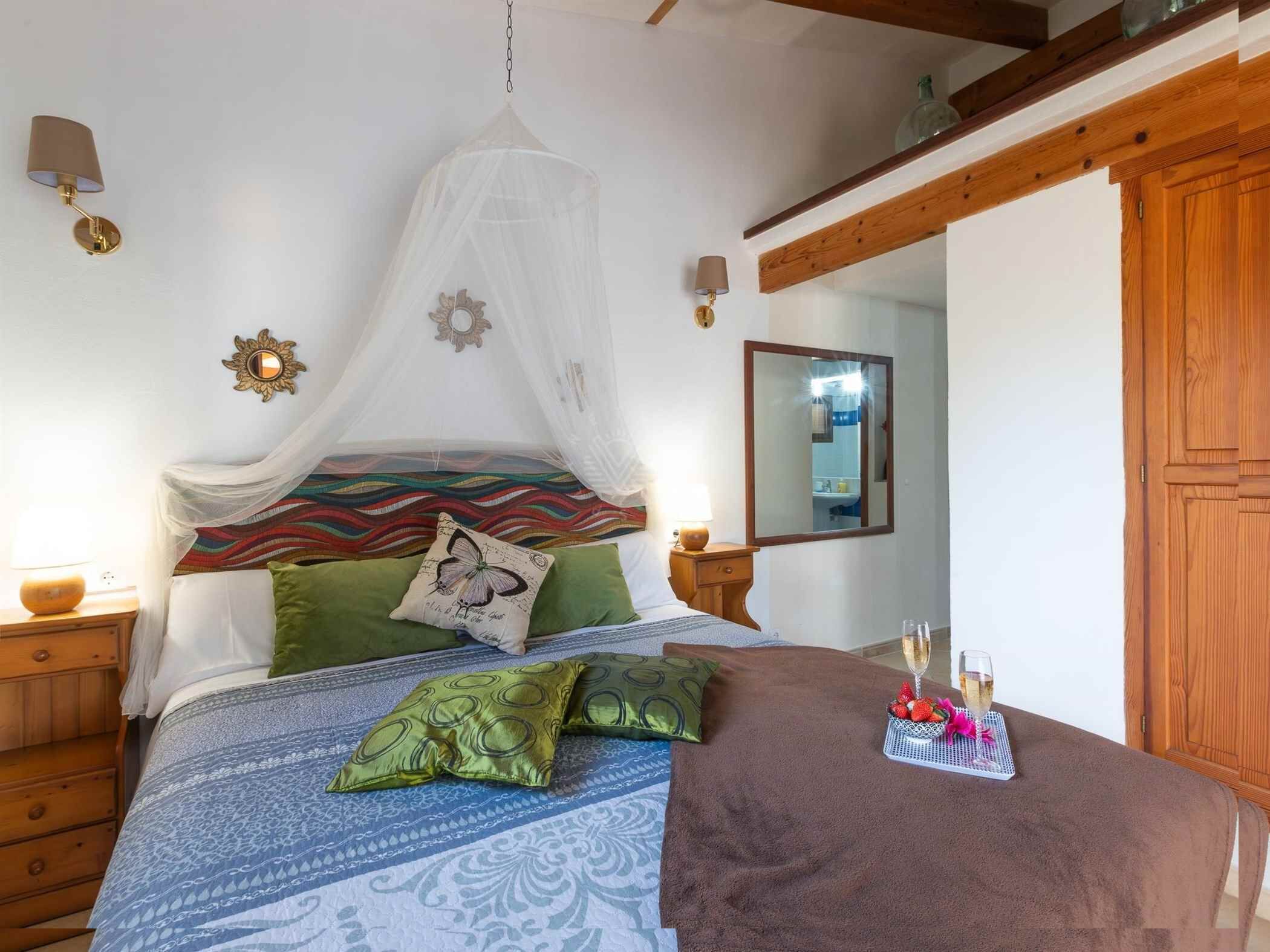 Een slaapkamer met een hemelbed, een nachtkastje met een lamp, een spiegel, en een dienblad met een drankje en aardbeien.