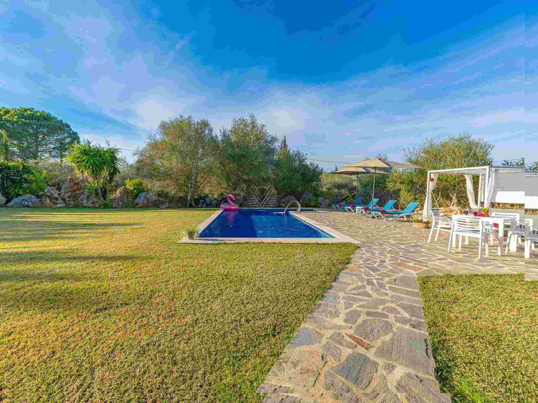 A swimming pool with a stone pathway leading to a seating area with umbrellas and chairs.