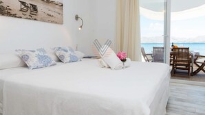 A hotel room with a large bed, a view of the sea, and a balcony with a table and chairs. - Ran de Mar, house directly on the beach with spectacular sea views (Alcúdia)