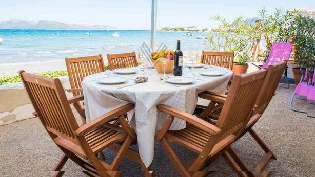 A round table with a white tablecloth, surrounded by wooden chairs, set on a patio with a view of the sea. - Ran de Mar, house directly on the beach with spectacular sea views (Alcúdia)