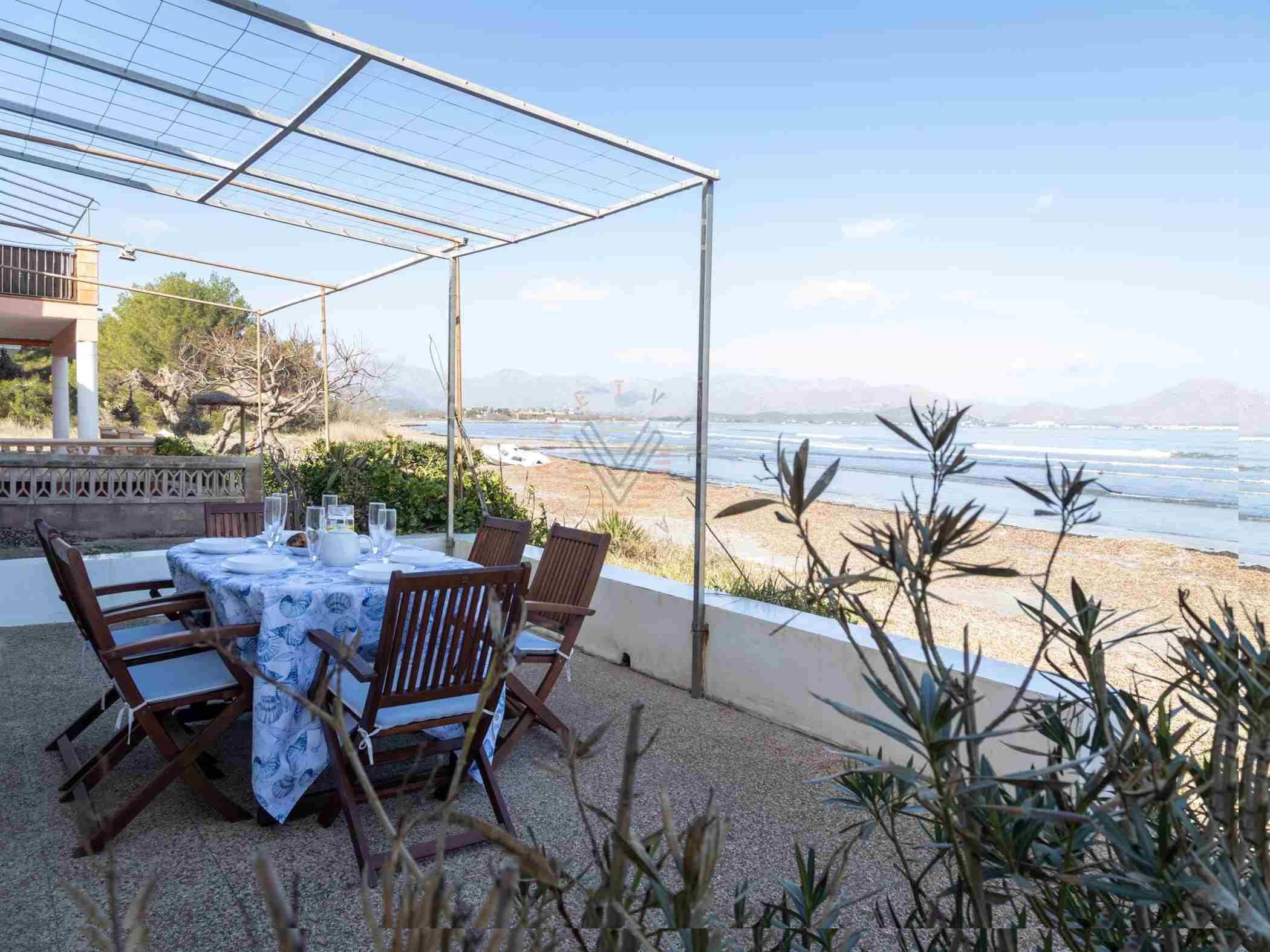 Zona d'aigüdegots a l'exterior amb una taula preparada per a quatre persones, amb vista a una platja i l'oceà.