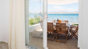 A balcony with a table set for dining, overlooking a beach with a clear view of the sea and distant mountains. - Ran de Mar, house directly on the beach with spectacular sea views (Alcúdia)