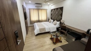Habitación de hotel con cama, escritorio, silla, mesita, ventilador de techo y televisor.