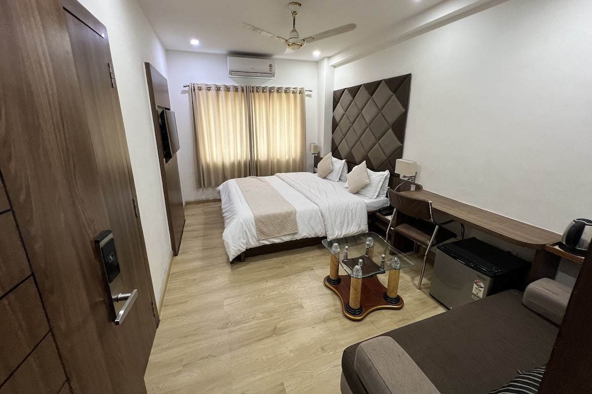 Une chambre d’hôtel équipée d’un lit, d’un bureau, d’une chaise, d’une petite table, d’un ventilateur de plafond et d’une télévision.