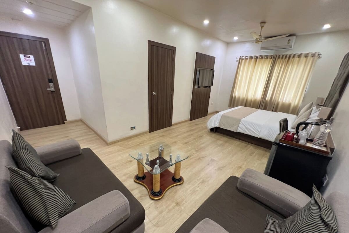 Une chambre d’hôtel comprenant un lit, deux canapés, une table basse, un bureau avec une lampe et une fenêtre avec des rideaux.