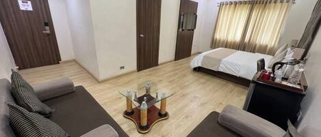 A hotel room with a bed, two sofas, a coffee table, a desk with a lamp, and a window with curtains.