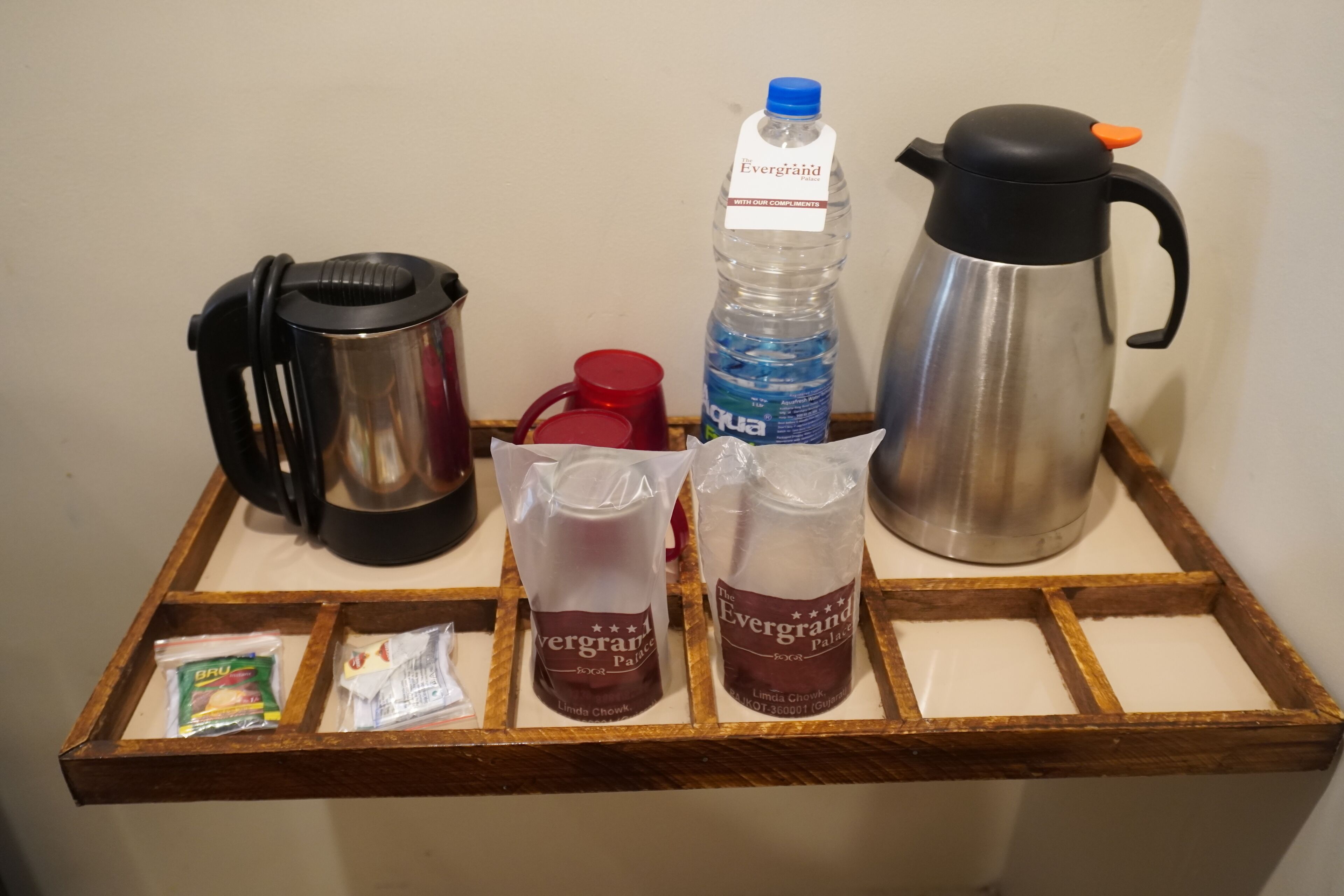 A wooden tray with a coffee maker, a water bottle, two bags of Evergrand Palate, a red mug, and a packet of GRU.