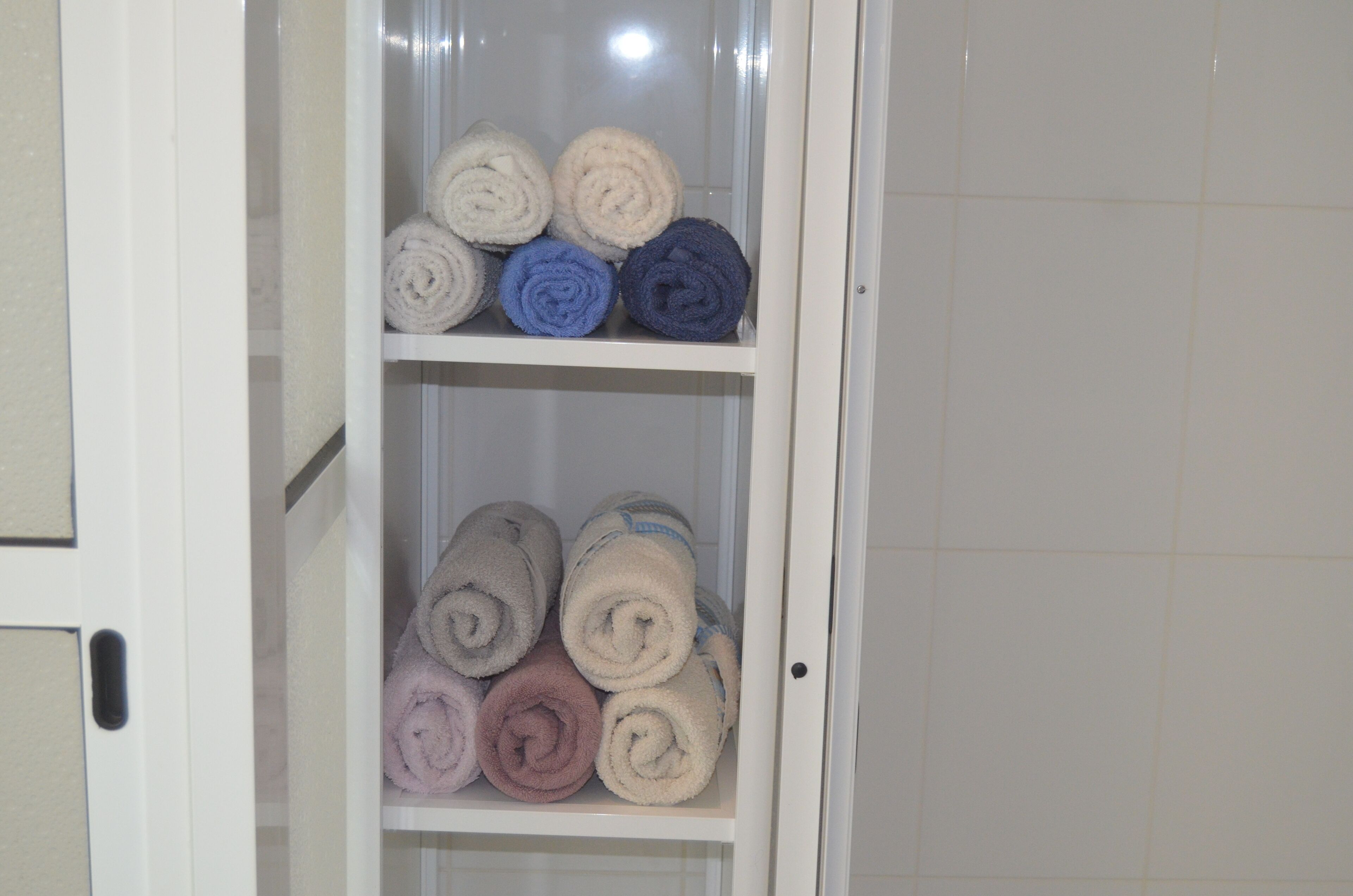 Un baño con cabina de ducha de vidrio y un perchero con toallas enrolladas en varios colores.