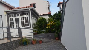 A residential area with a tiled patio, potted plants, and a white building with a tiled roof. - ATLANTIC HOUSE WITH CAR AND BIKE (Câmara de Lobos)