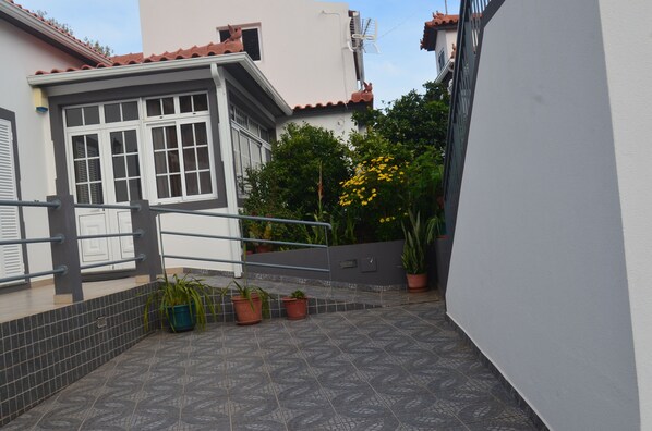 Un quartier résidentiel avec une terrasse carrelée, des plantes en pot et un bâtiment blanc doté d’un toit en tuiles.