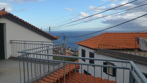 A residential area with terracotta roofs, a balcony with a metal railing, and a view of the sea. - ATLANTIC HOUSE WITH CAR AND BIKE (Câmara de Lobos)