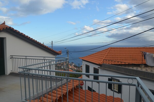 A residential area with terracotta roofs, a balcony with a metal railing, and a view of the sea. - ATLANTIC HOUSE WITH CAR AND BIKE (Câmara de Lobos)