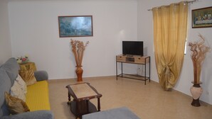 A living room with a sofa, a coffee table, a TV on a stand, a painting on the wall, and a curtain. - ATLANTIC HOUSE WITH CAR AND BIKE (Câmara de Lobos)