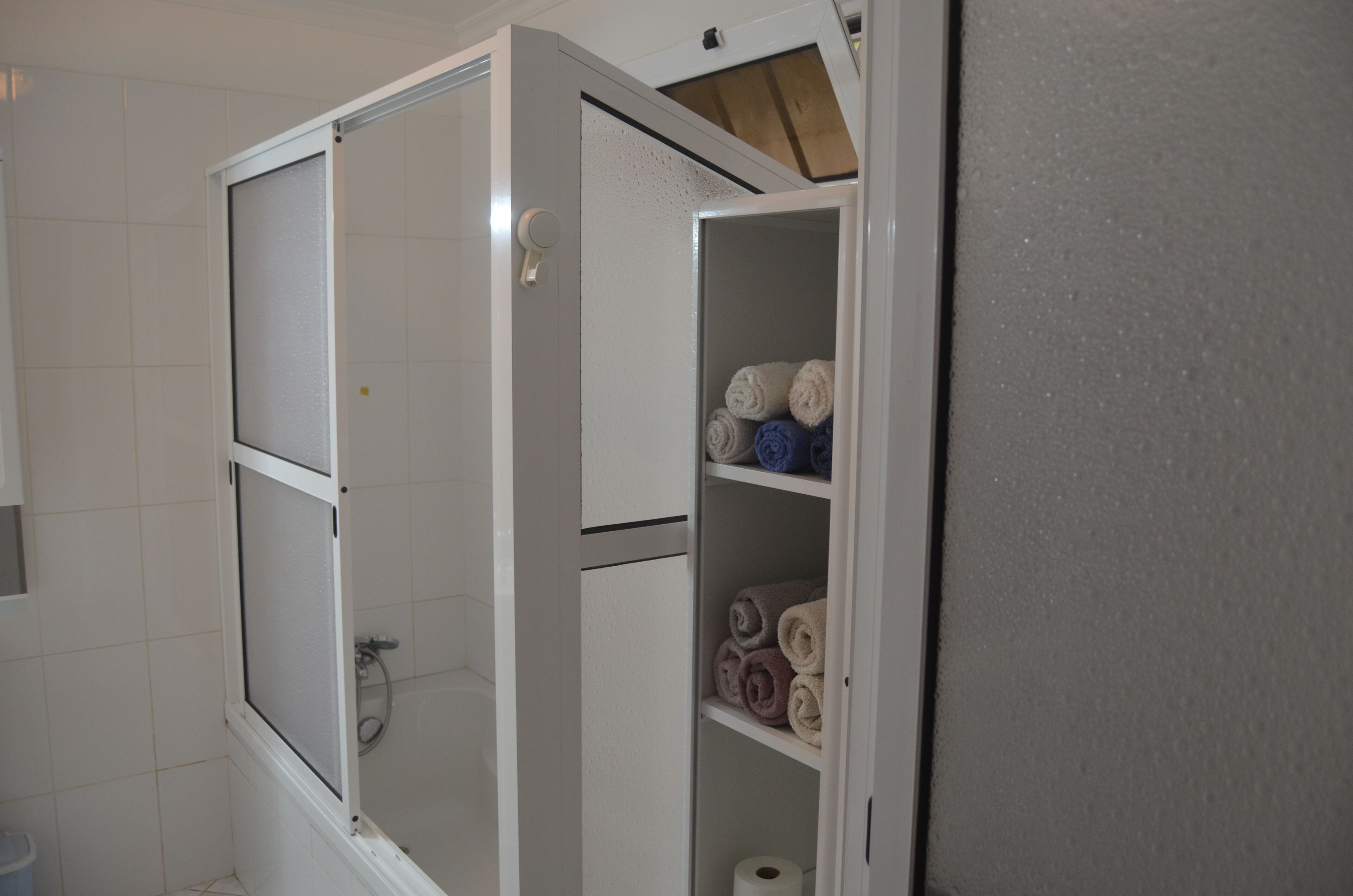 Een badkamer met een douchecabine, toilet en een handdoekrek met handdoeken.