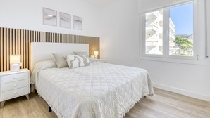 A bedroom with a bed, bedside tables, a window, and a view of buildings.