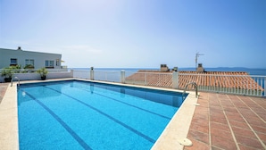 A rectangular swimming pool with clear blue water, surrounded by a tiled deck and a white fence.
