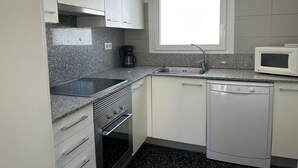 A compact kitchen with white cabinets, a built-in oven, a dishwasher, a coffee maker, and a microwave. - Agi Joan Badosa 2 Apartamento for rent in Roses Girona. (Roses)