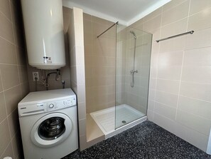 A compact bathroom with a washing machine, a glass-enclosed shower, and tiled walls. - Agi Joan Badosa 2 Apartamento for rent in Roses Girona. (Roses)