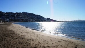 A beach with a clear sky, calm sea, and a hilly backdrop with buildings. - Agi Joan Badosa 2 Apartamento for rent in Roses Girona. (Roses)