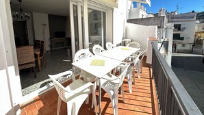 An outdoor balcony with a white table and chairs, a wicker sofa, and a television in the background. - Agi Joan Badosa 2 Apartamento for rent in Roses Girona. (Roses)