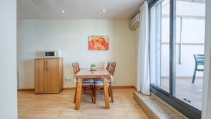 A dining area with a wooden table and chairs, a microwave on a cabinet, and a painting of fruit on the wall. - P.C. GREGAL 4 ATICO Roses (Rosas / Roses)