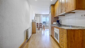 A kitchen with wooden cabinets, a granite countertop, and a view to a balcony. - P.C. GREGAL 4 ATICO Roses (Rosas / Roses)