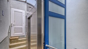 A staircase with a metal railing, a white door with horizontal slats, and a blue door with a frosted glass panel. - P.C. GREGAL 4 ATICO Roses (Rosas / Roses)