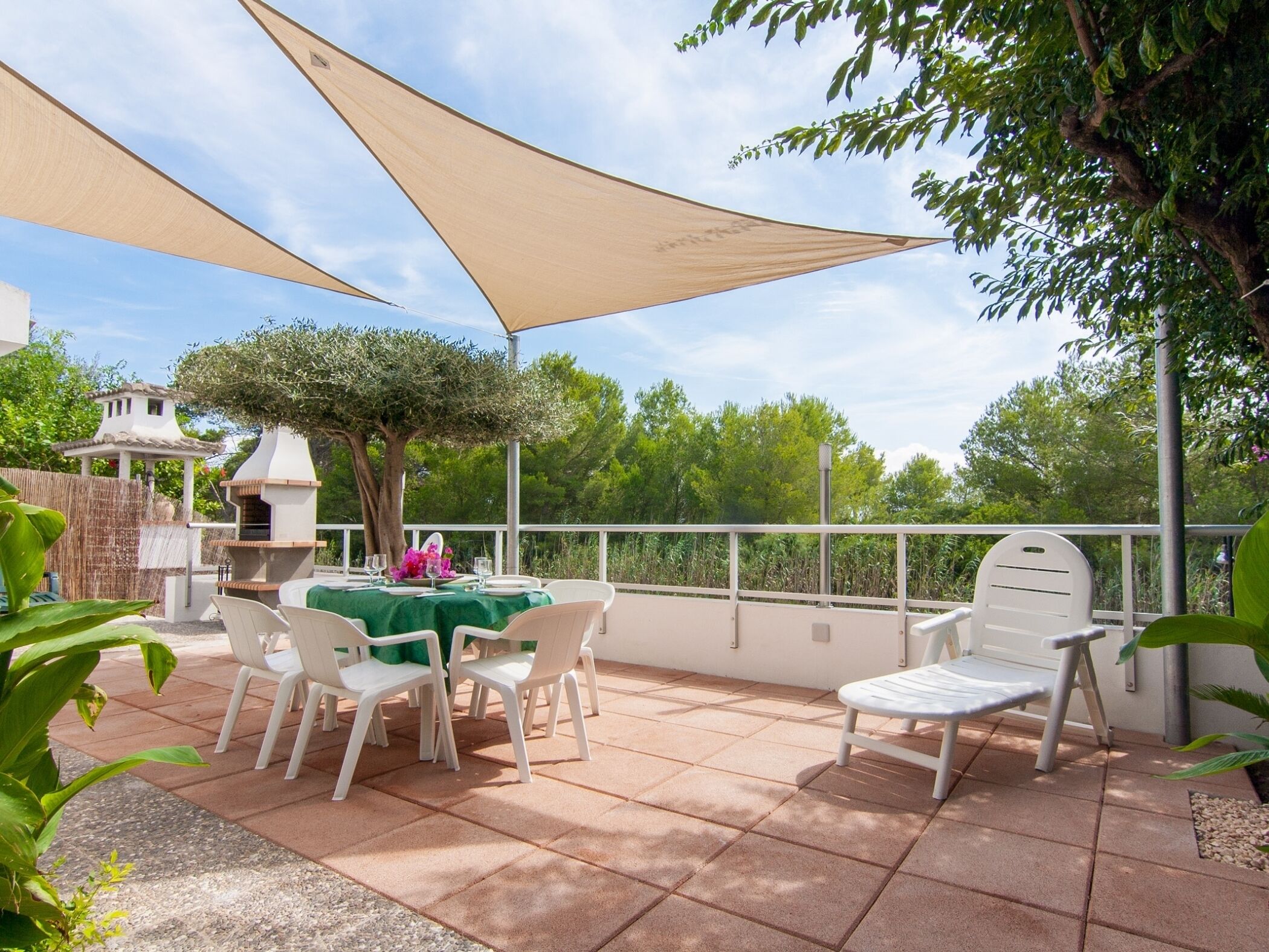 An outdoor patio with a table set for dining, surrounded by white chairs, under large beige canopies.