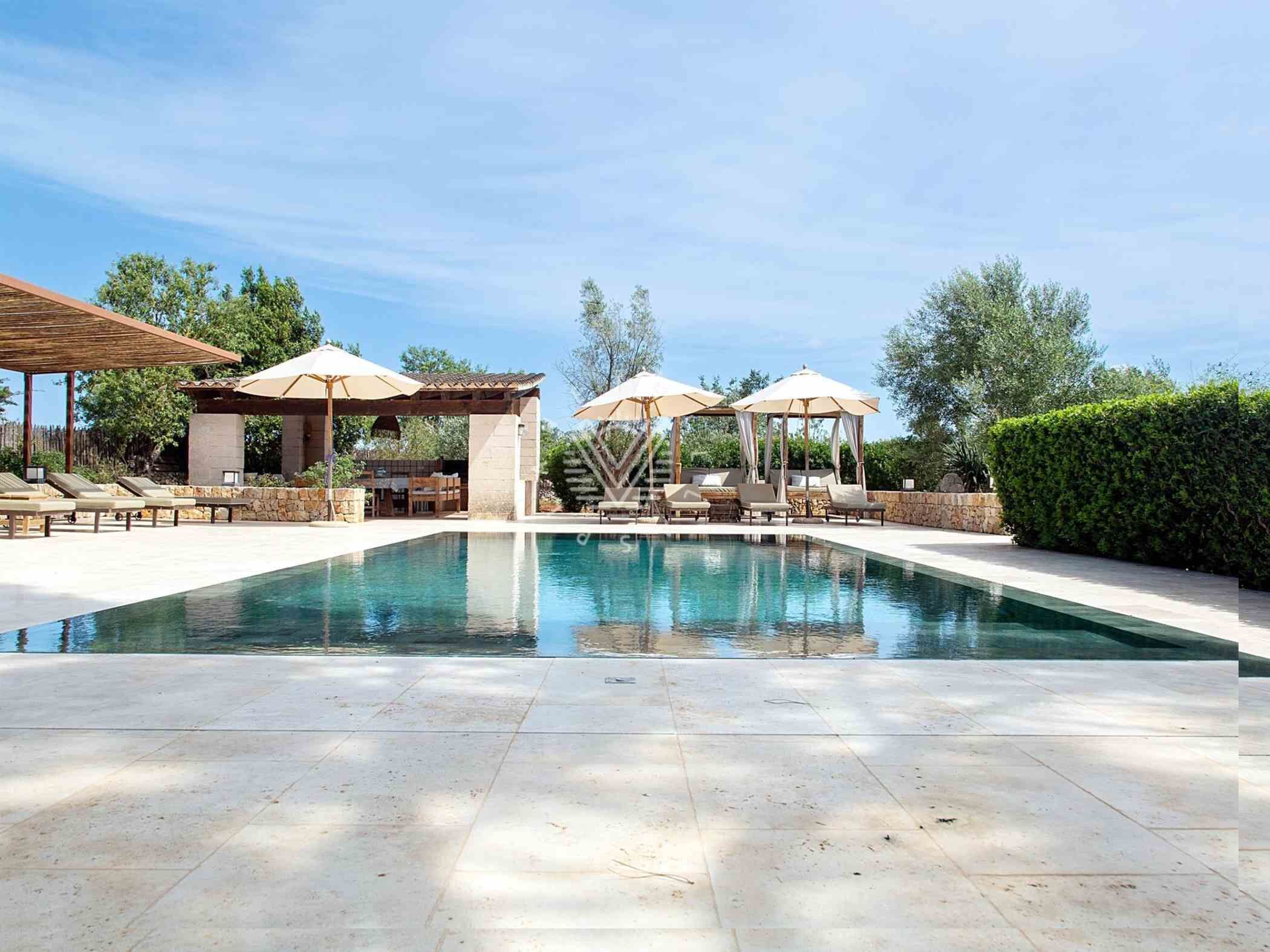 A swimming pool with lounge chairs and umbrellas, surrounded by stone structures and greenery.