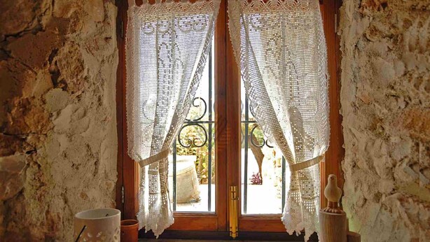 A rustic room with a wooden door, white lace curtains, a metal gate, and a rustic stone wall. - Figuera Blanca (Buger)