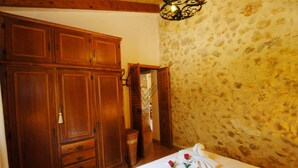 A bedroom with a large wooden wardrobe, a stone wall, and a chandelier. - Figuera Blanca (Buger)