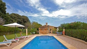 A swimming pool with lounge chairs and an umbrella, surrounded by greenery and a stone building. - Figuera Blanca (Buger)