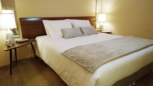 A neatly made bed with white and striped pillows, a beige blanket, and two bedside lamps on wooden nightstands. - QUAD 2 with Balcony, Garage, A.C. (Cold or heat), 24/7 security  (Lisboa)