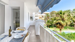 A balcony with a table set for dining, a bottle of wine, and a view of a swimming pool and palm trees. - ROYAL MARINE 2 240 Roses (Rosas / Roses)