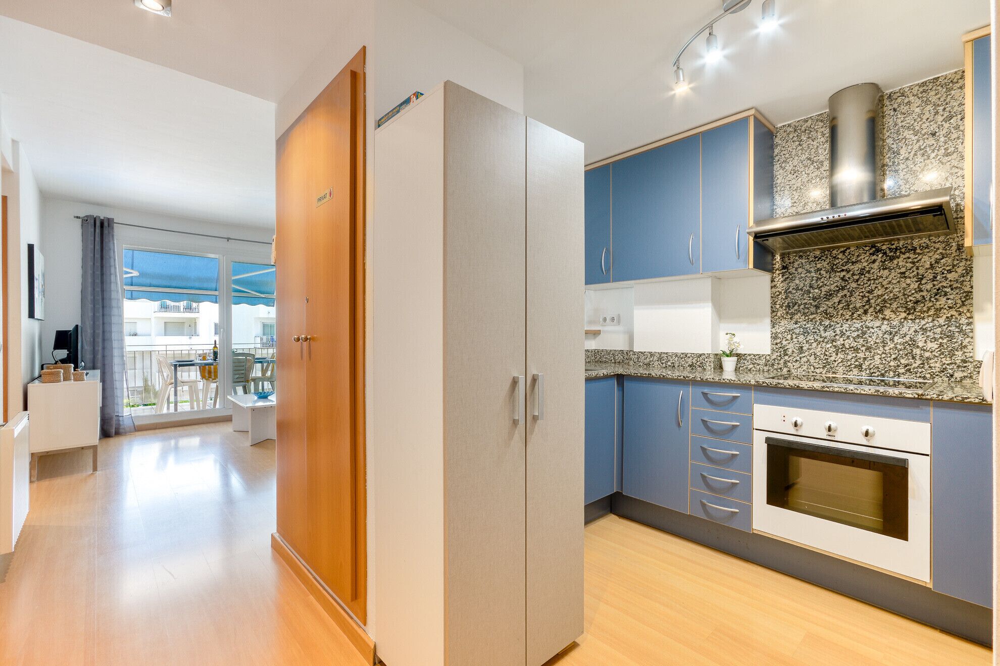 A modern kitchen with blue cabinets, a stainless steel range hood, and a built-in oven.