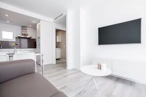 Un salon moderne avec un canapé gris, une petite table blanche et un téléviseur à écran plat fixé au mur.