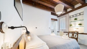 Un dormitorio con cama, lámpara de noche, vigas de madera, una ventana y una estantería con plantas.