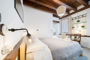 Une chambre à coucher avec un lit, une lampe de chevet, des poutres en bois, une fenêtre et une étagère avec des plantes.