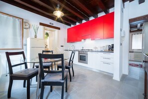 A modern kitchen with red cabinets, a dining area with a glass table, and a visible clock on the wall. - Ve.N.I.Ce. Cera Casa Santo Stefano (Venezia)