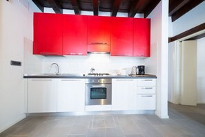 A modern kitchen with white cabinets, a stainless steel oven, and a red upper cabinet. - Ve.N.I.Ce. Cera Casa Santo Stefano (Venezia)