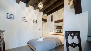 A bedroom with a bed, a chair, a shelf with items, and a framed picture on the wall. - Ve.N.I.Ce. Cera Casa Santo Stefano  (Venezia)