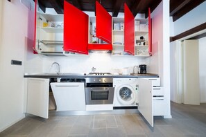 Une cuisine compacte avec des meubles blancs, un four encastré, un lave-linge et une machine à café.