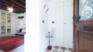 Una habitación con una puerta blanca, un radiador, piso de tablones de ajedrez, una estantería y una alfombra roja.
