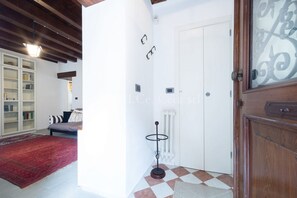 Une pièce avec une porte blanche, un radiateur, un sol à carreaux, une bibliothèque et un tapis rouge.