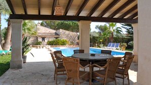 A covered outdoor area with a stone floor, a round table with chairs, and a pool in the background. - Ses Rodes, holiday villa in Porto Colom, Mallorca (Felanitx)