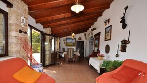 A cozy room with two red sofas, a stone wall, wooden ceiling beams, and a dining area with a table and chairs. - Ses Rodes, holiday villa in Porto Colom, Mallorca (Felanitx)